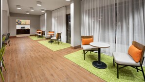 A hotel lobby with a dining area, a kitchen in the background, and a large window with sheer curtains. - Spark by Hilton Decatur (Decatur)