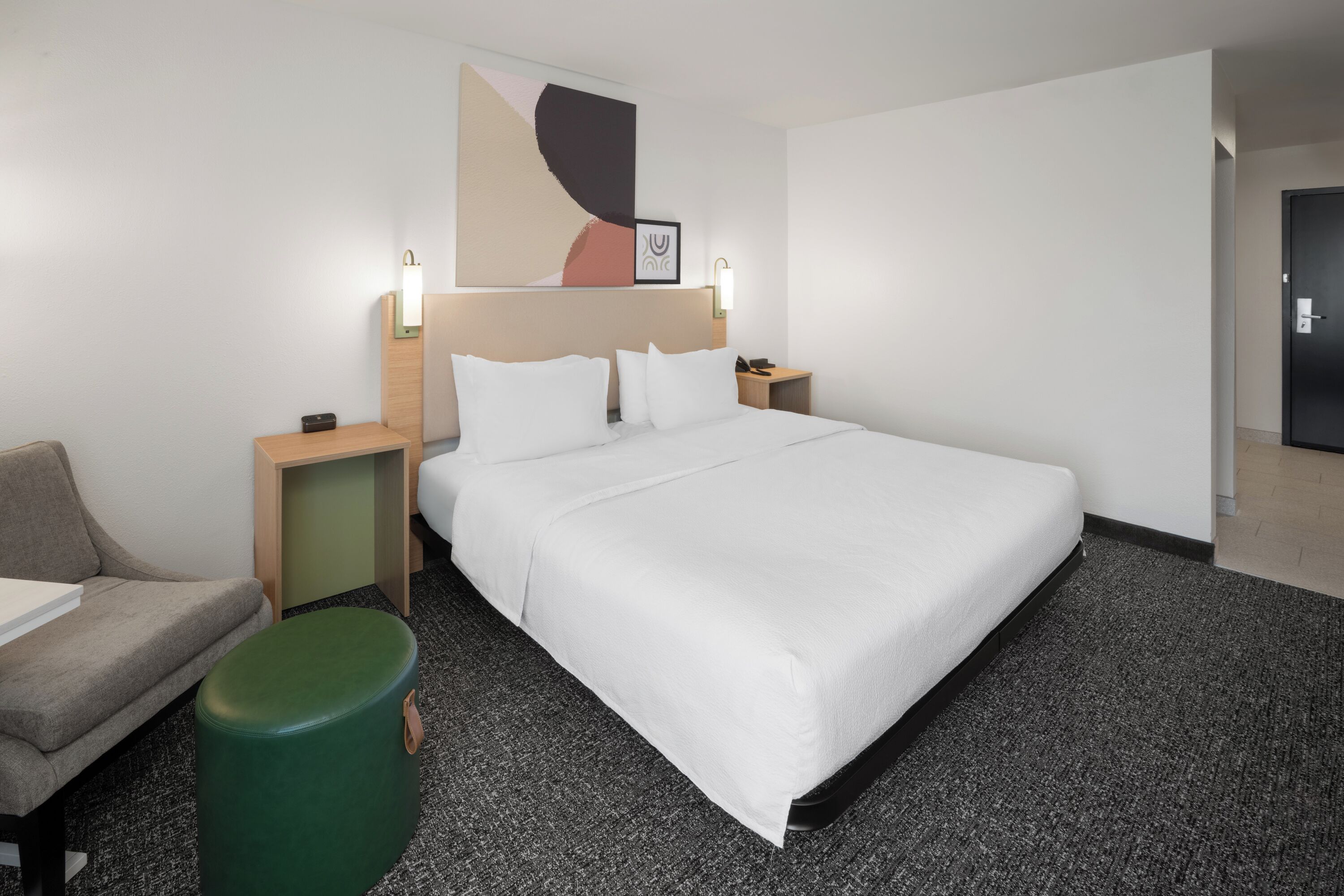 A hotel room with a large bed, a desk, a chair, and a green ottoman.