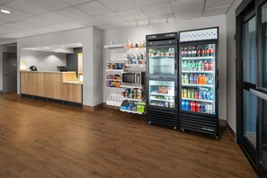 A reception area with a wooden counter, a refrigerator stocked with beverages, and a microwave. - Spark by Hilton Decatur (Decatur)