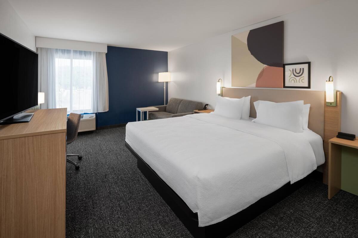 A hotel room with a large bed, a desk, a chair, a TV, and a window with curtains.