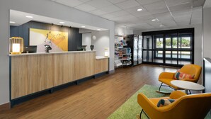 A reception area with a wooden reception desk, a computer, a phone, and a small seating area with two chairs and a table. - Spark by Hilton Decatur (Decatur)