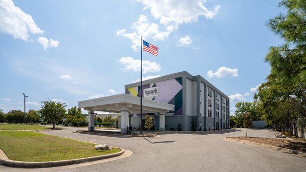 A hotel entrance with a covered parking area, a flag, and a building with a 'spark by Hilton' sign.
