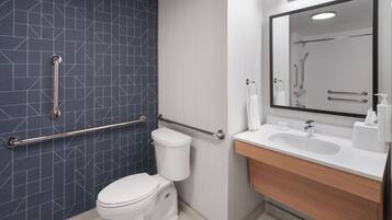 Ein modernes Badezimmer mit geometrischer Fliesenrückwand, einer weißen Toilette, einem Waschbecken mit Spiegel und Haltegriffen.