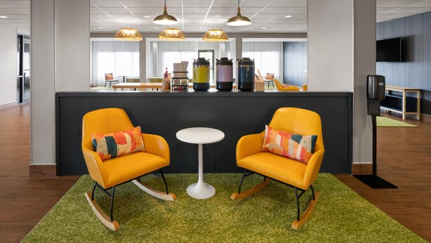 A modern hotel lobby with a central bar area, two rocking chairs, a small round table, and a green carpet. - Spark by Hilton Decatur (Decatur)