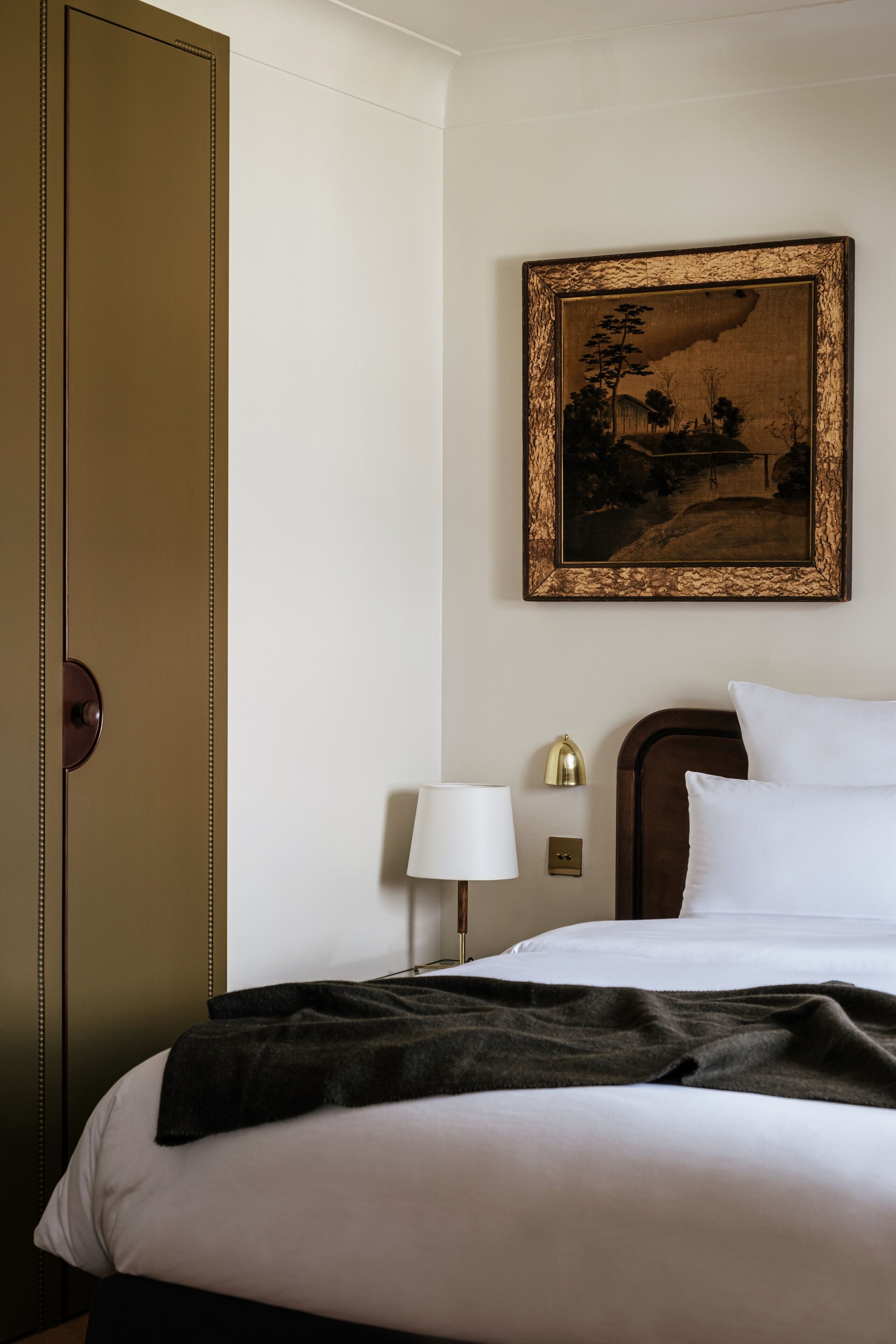 Una habitación de hotel con una cama, una mesita de noche, una lámpara, un cuadro enmarcado y un armario.