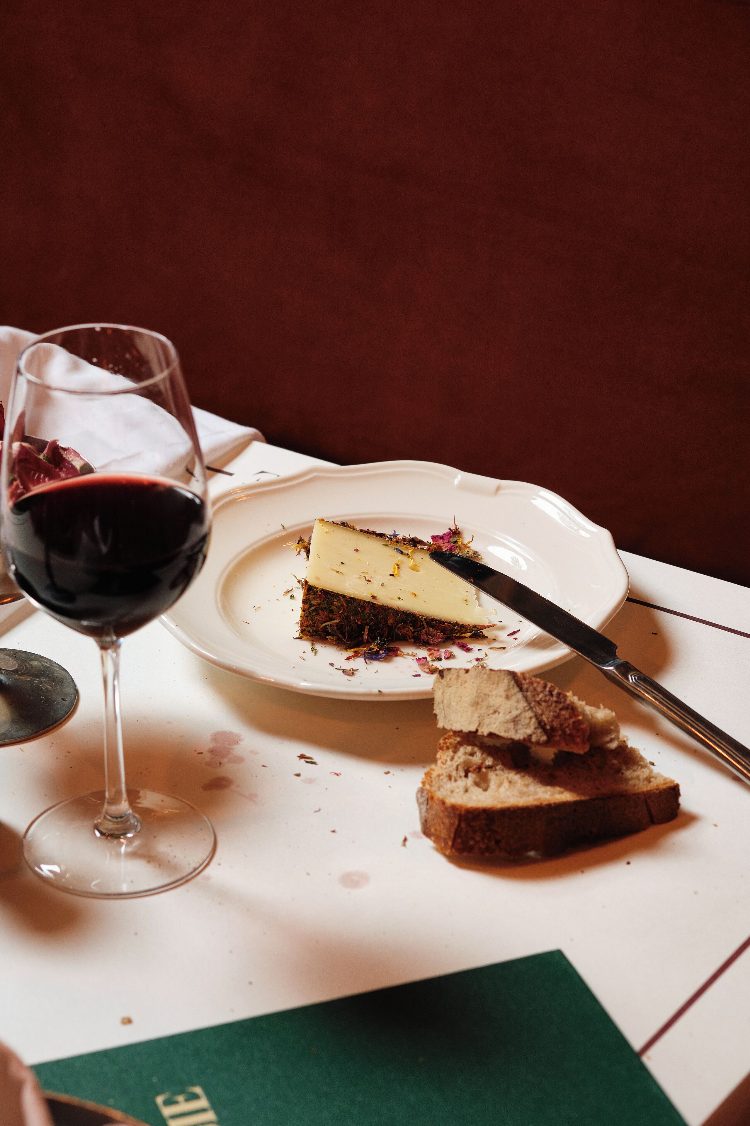 Une part de gâteau au fromage sur une assiette, avec un couteau à côté, et un verre de vin rouge.