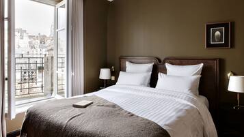Habitación de hotel con una cama grande, vistas de la ciudad a través de una ventana y un cuadro enmarcado en la pared.