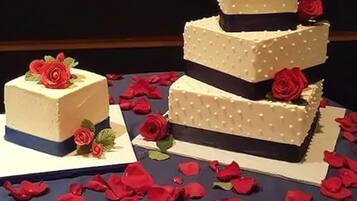 A multi-tiered cake with white frosting and red roses on top, placed on a table with red rose petals scattered around.