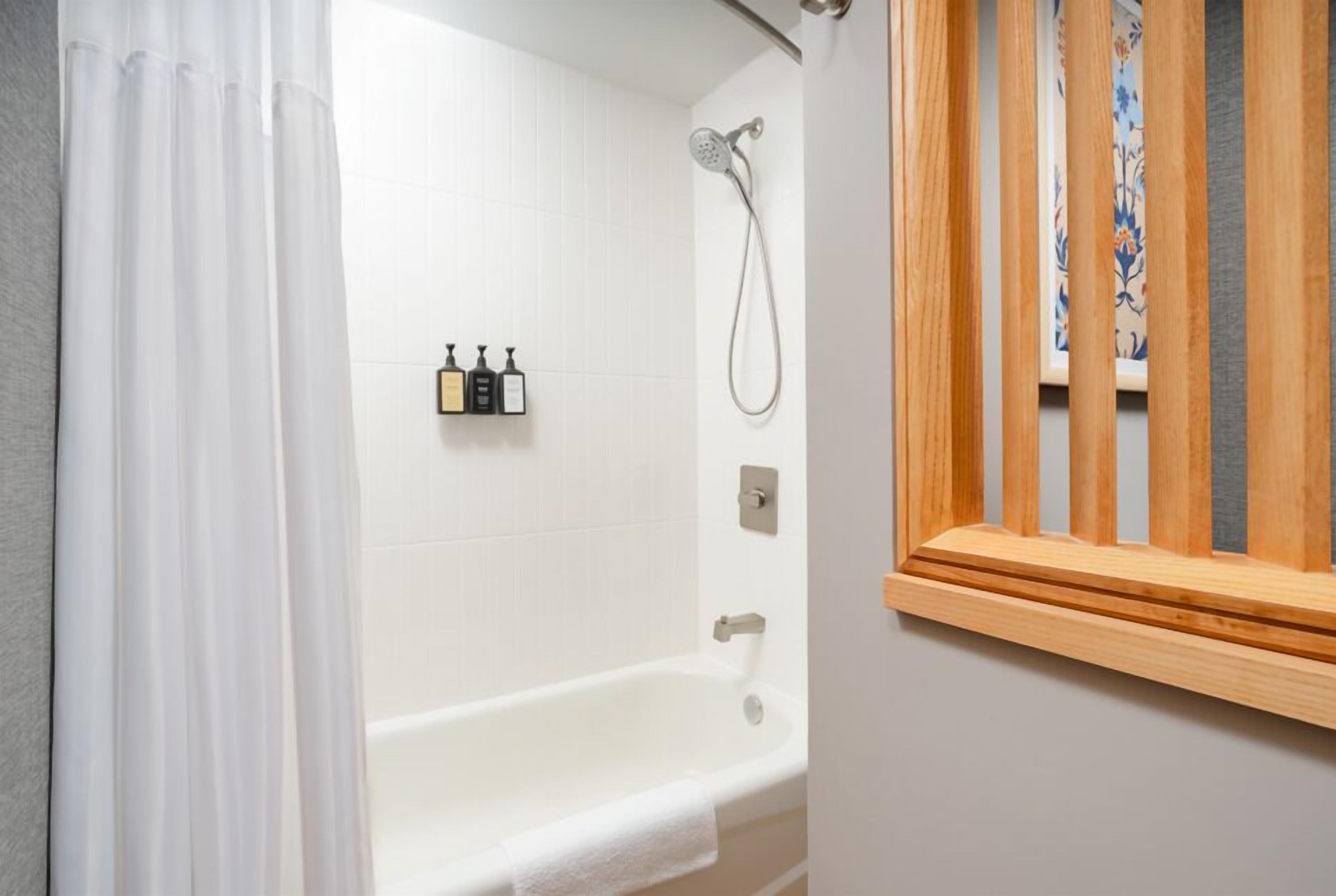 A bathroom with a bathtub, shower, and three bottles of toiletries on the wall.