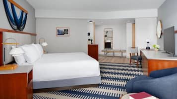 Quarto de hotel com cama, mesa de cabeceira, luminária e um sofá azul.