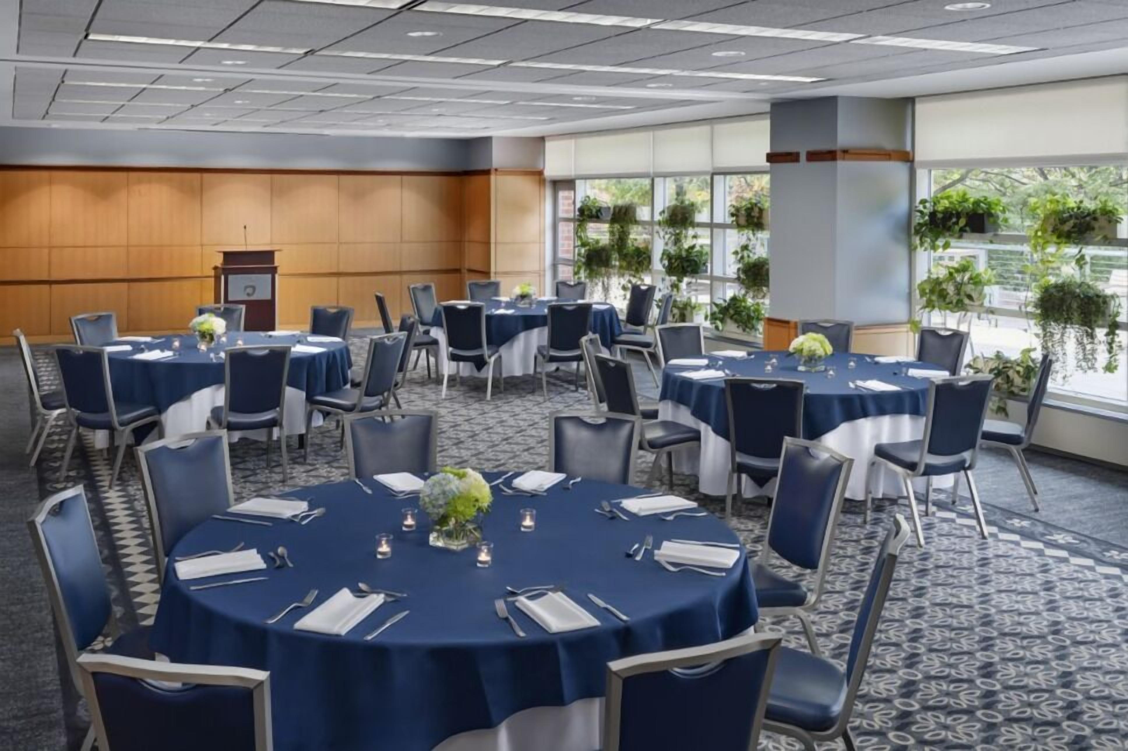 Une salle de conférence équipée de tables rondes, de chaises et d’un pupitre.