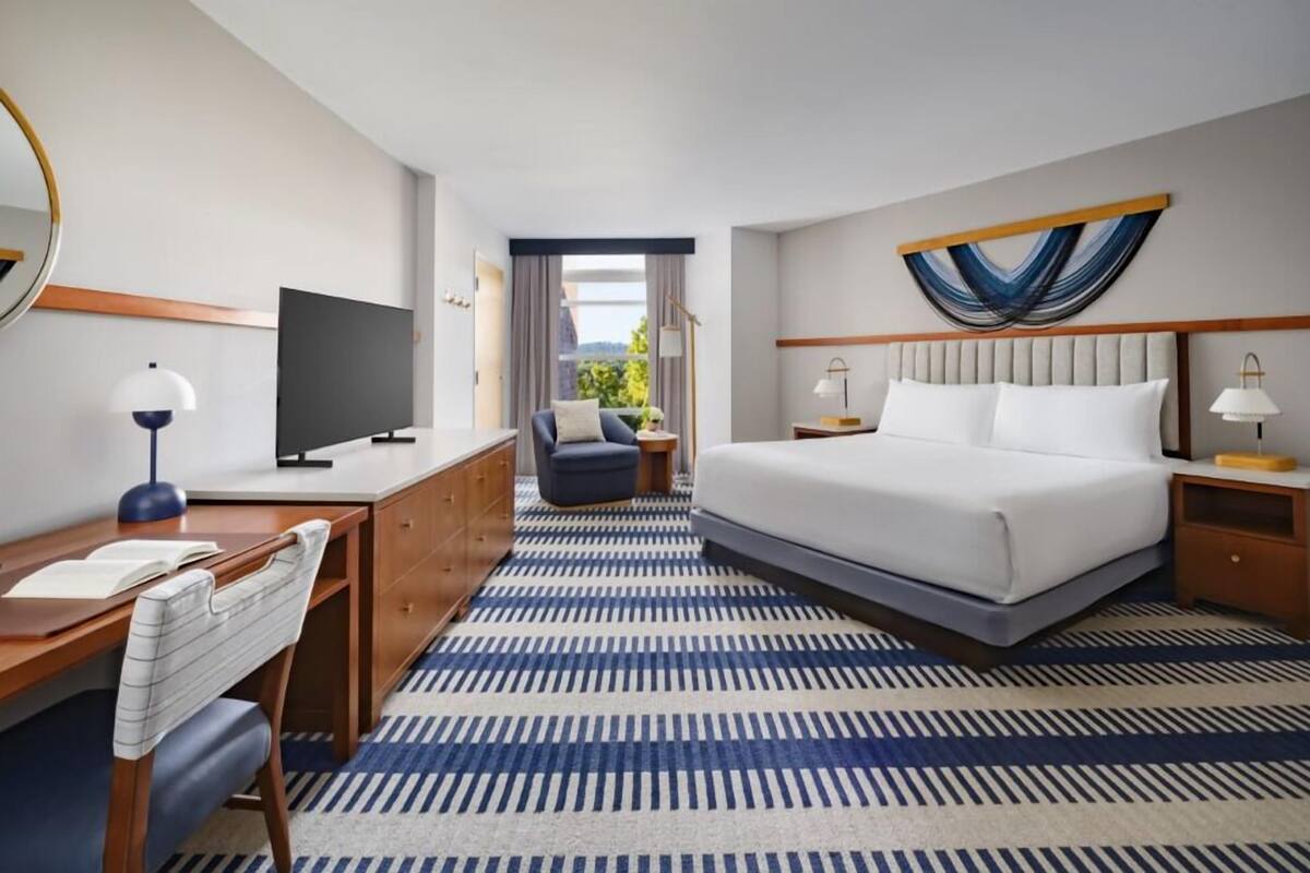 A hotel room with a large bed, a desk with a computer, a chair, and a view of the outdoors.