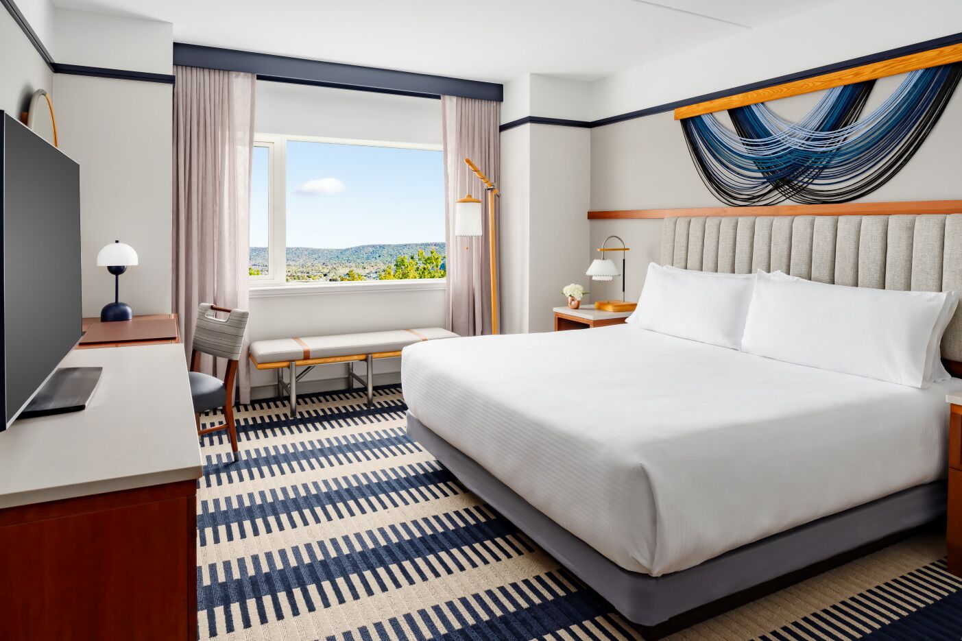 Une chambre d’hôtel comprenant un lit, un bureau, une chaise, une fenêtre avec vue et une œuvre d’art murale.