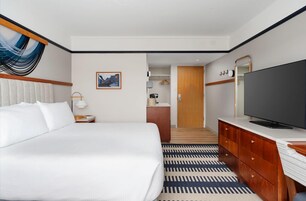 Una habitación de hotel con una cama grande, televisión, cómoda de madera, escritorio y alfombra estampada.