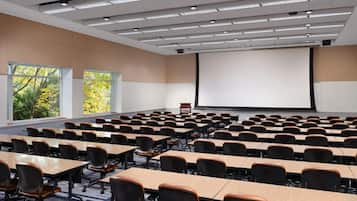 A conference room with rows of tables and chairs, large windows, and a projection screen.