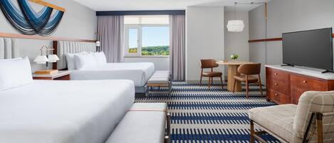 Habitación de hotel con dos camas, un escritorio con silla, televisor y una ventana grande con vistas.