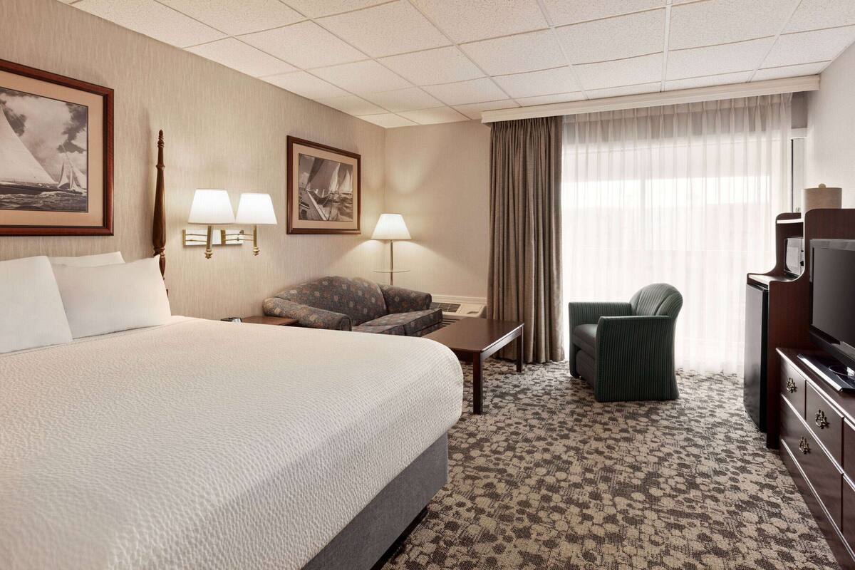 A hotel room with a large bed, two bedside lamps, a sofa, a television, and a desk.