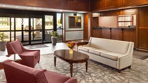 A lobby with a reception desk, a sofa, two armchairs, a coffee table, and a potted plant. - Ramada Plaza by Wyndham Portland (Portland)