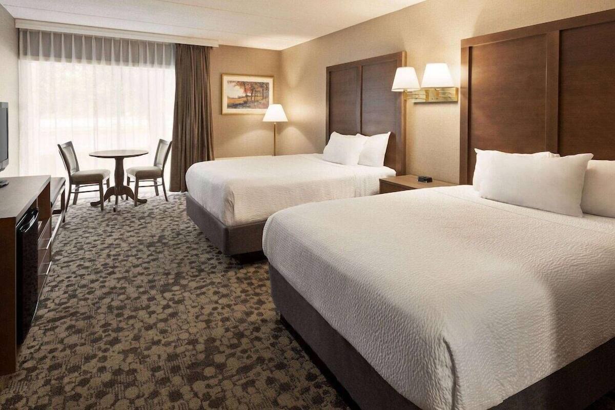 A hotel room with two beds, a desk, a chair, a small table, and a painting on the wall.