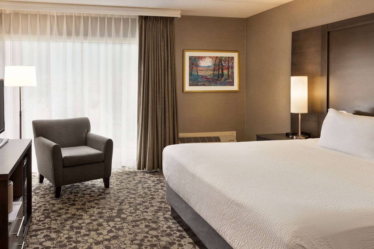 A hotel room with a large bed, a chair, a desk, and a painting on the wall.