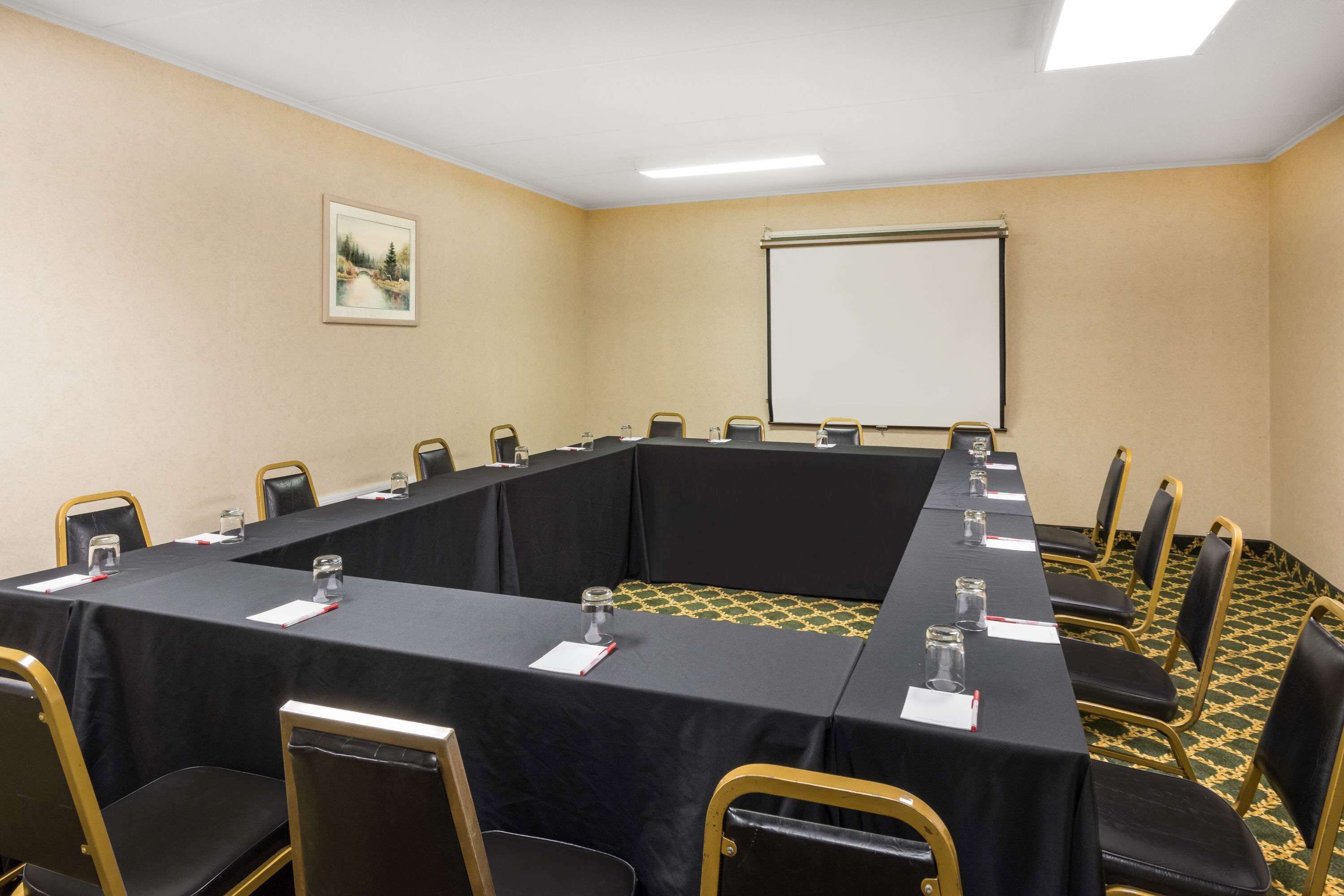 A conference room with a long table, black chairs, and a projector screen.