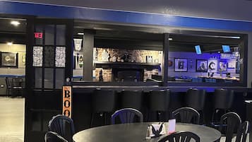 A restaurant with round tables and black chairs, a bar area with a stone wall, and an exit sign.