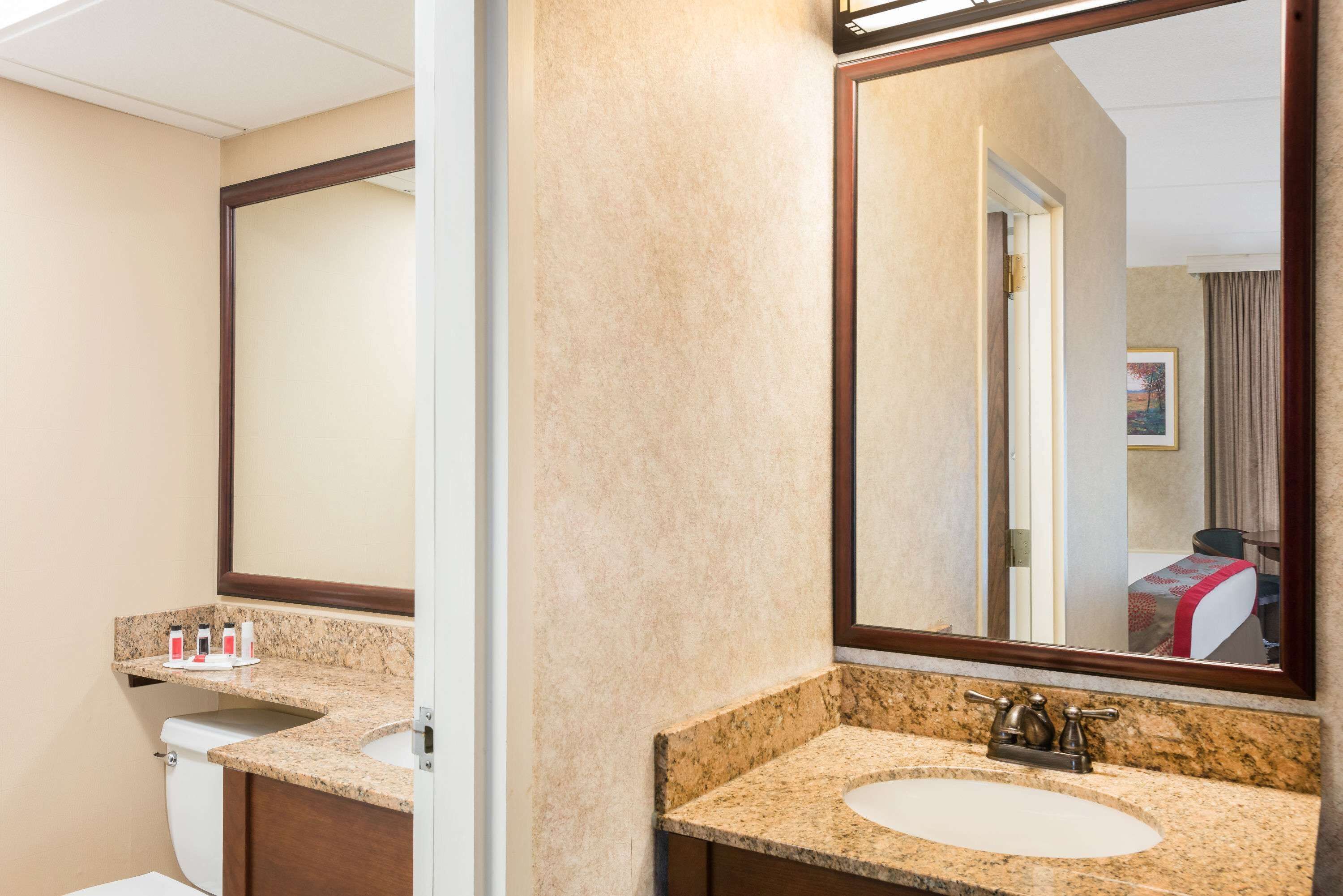 A hotel bathroom with two sinks, a large mirror, and a toilet.