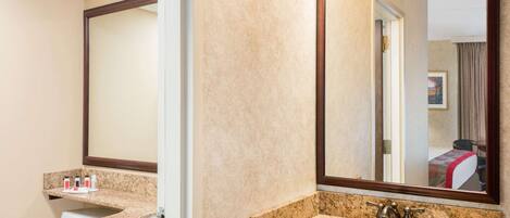 A hotel bathroom with two sinks, a large mirror, and a toilet.