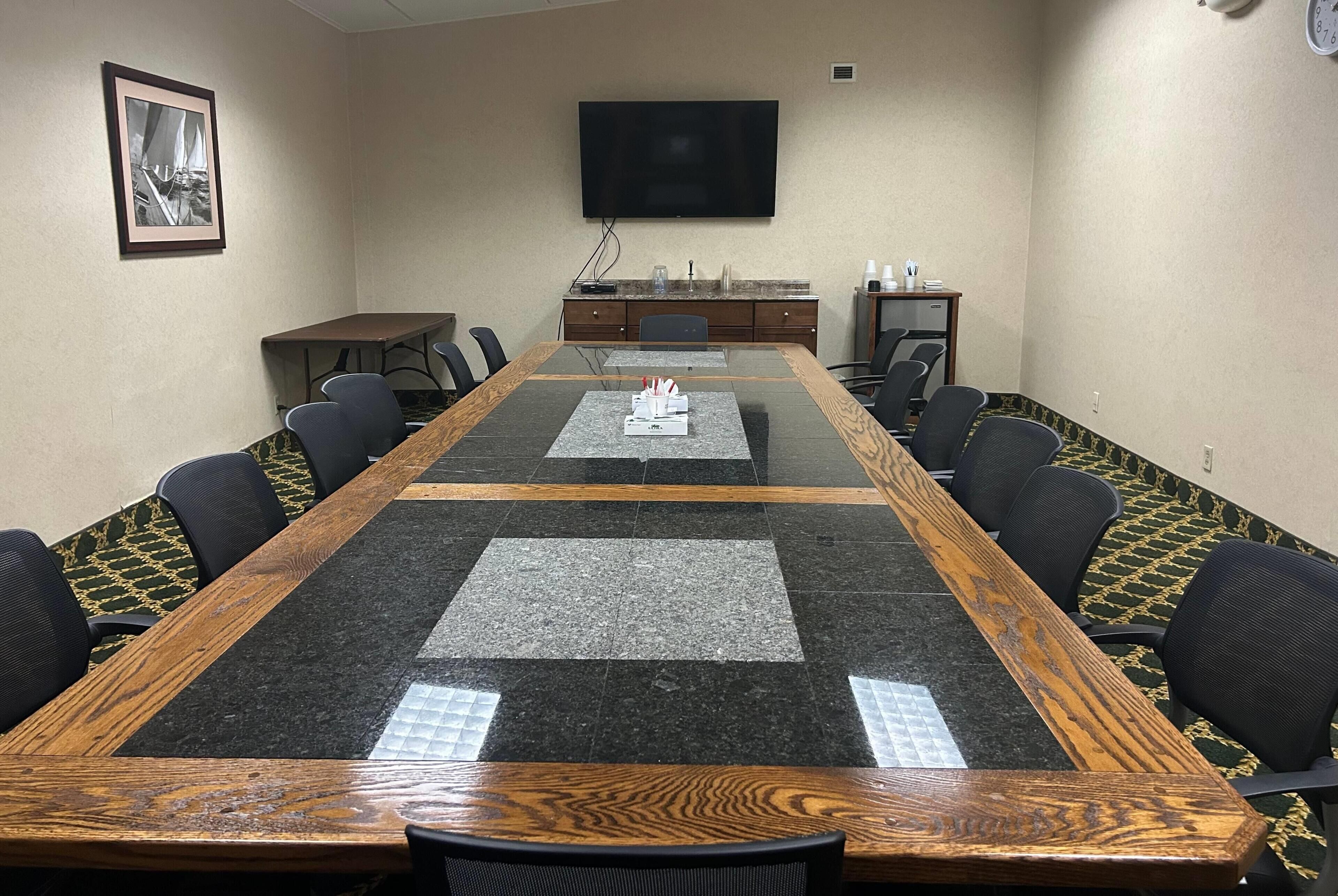 Une salle de conférence avec une longue table, des chaises, un téléviseur et une horloge au mur.