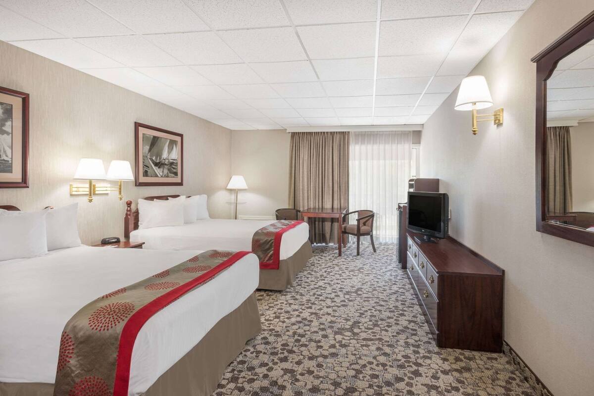 A hotel room with two beds, a desk, a television, and a mirror.