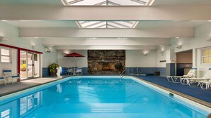 An indoor swimming pool with clear blue water, a stone fireplace, and lounge chairs. - Ramada Plaza by Wyndham Portland (Portland)