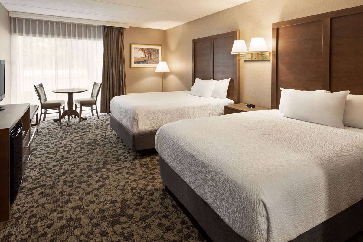 A hotel room with two beds, a desk, a chair, a small table, and a painting on the wall.