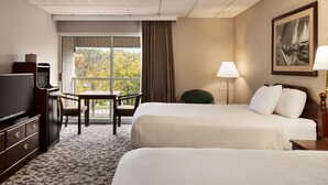 A hotel room with two beds, a desk with a chair, a television, and a window with a view of trees. - Ramada Plaza by Wyndham Portland (Portland)