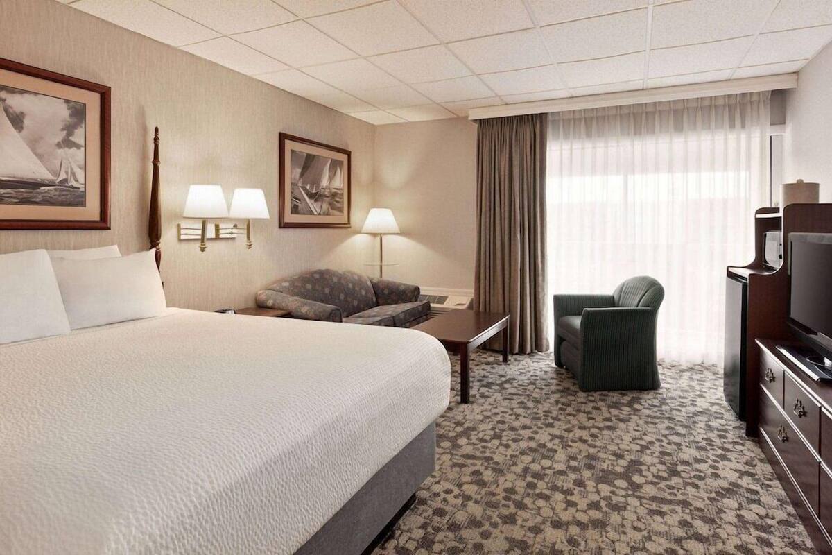 A hotel room with a large bed, two bedside lamps, a desk with a chair, a television, and a window with curtains.