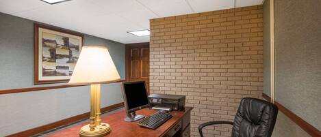 A hotel room with a wooden desk, a computer, a chair, a lamp, and a framed picture on the wall.