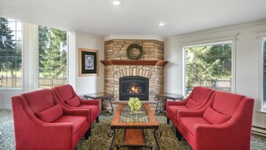 A room with a stone fireplace, two red armchairs, a coffee table, and patterned carpet. - Best Western Country Lane Inn (Juneau)