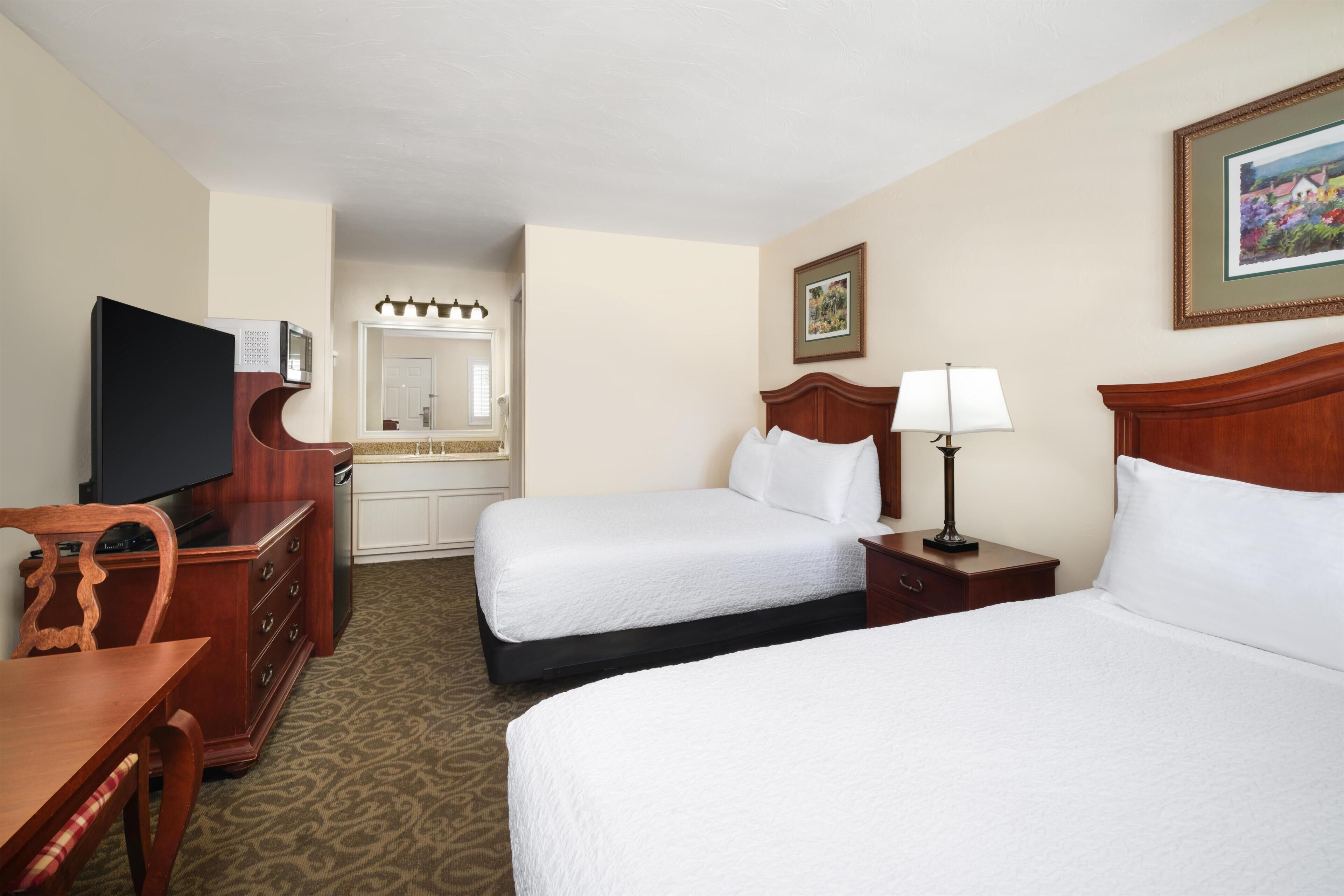 A hotel room with two beds, a television, a desk, and a dresser.