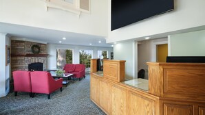A spacious living area with a fireplace, red sofas, a wooden cabinet, and a mounted TV. - Best Western Country Lane Inn (Juneau)