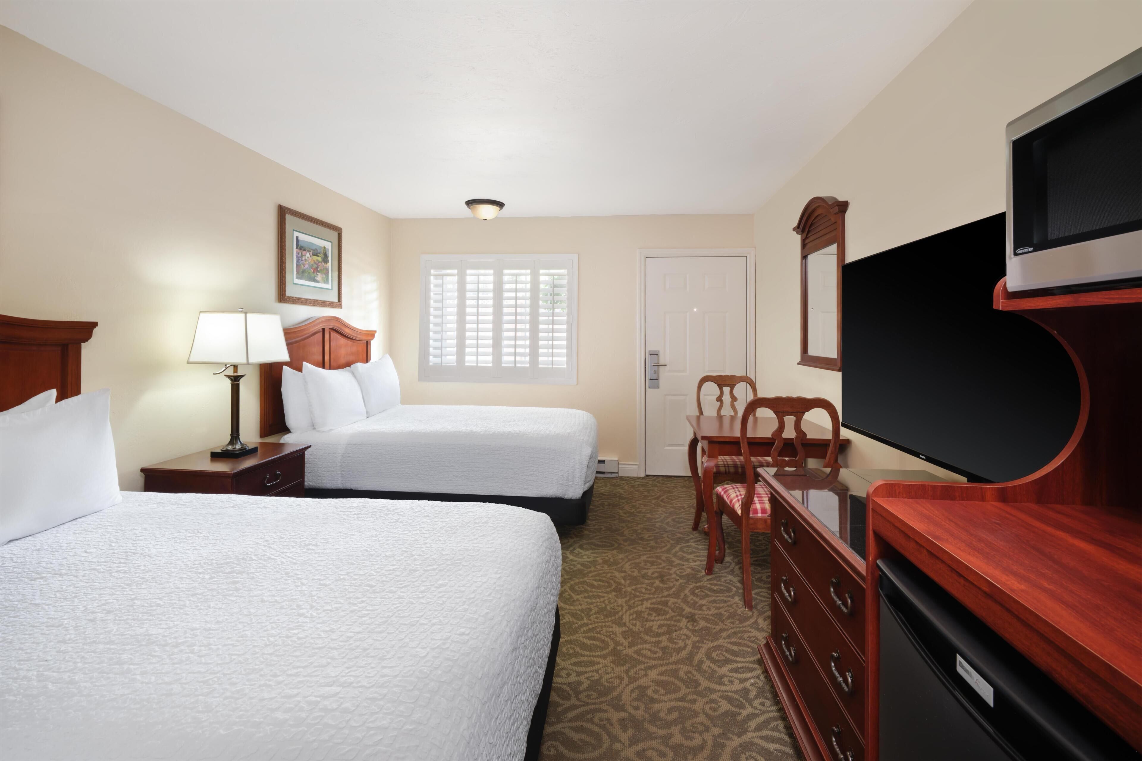 A hotel room with two beds, a TV, a desk, and a chair.