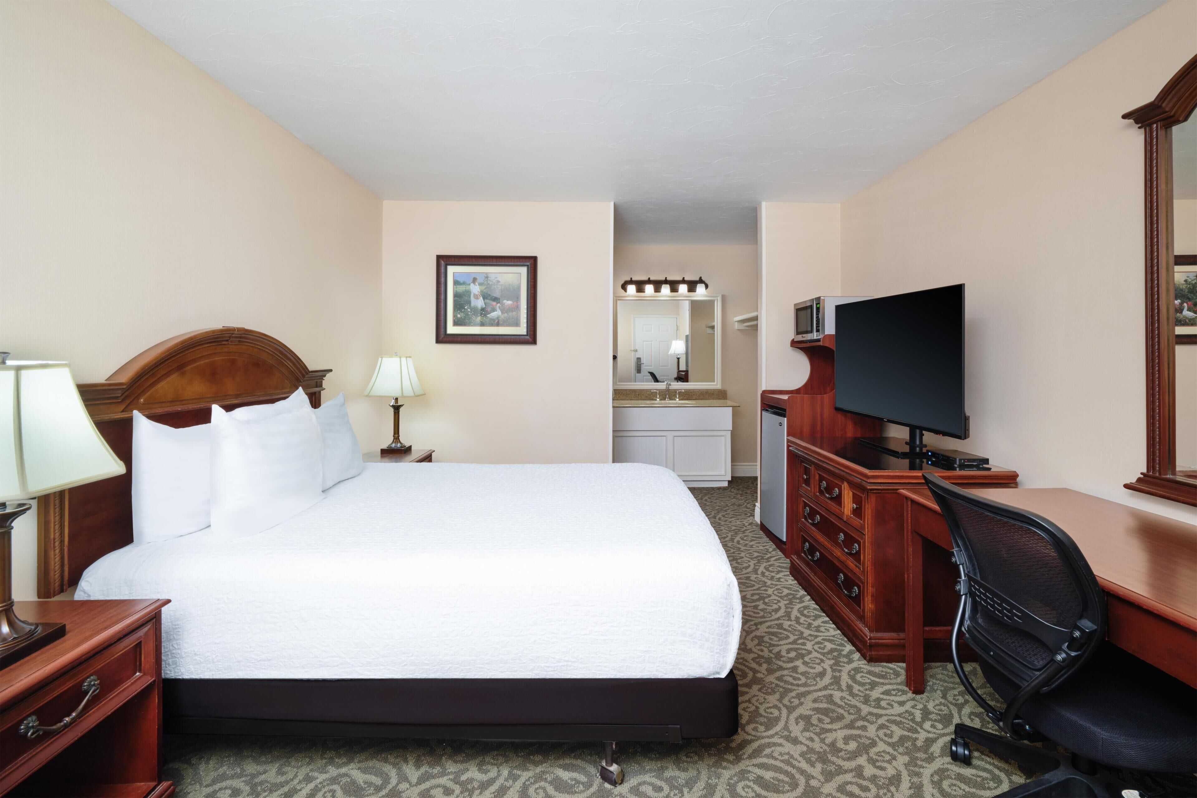 Habitación de hotel con una cama grande, un escritorio con computadora, televisor, cómoda y espejo.