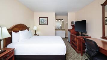 Habitación de hotel con una cama grande, un escritorio con computadora, televisor, cómoda y espejo.