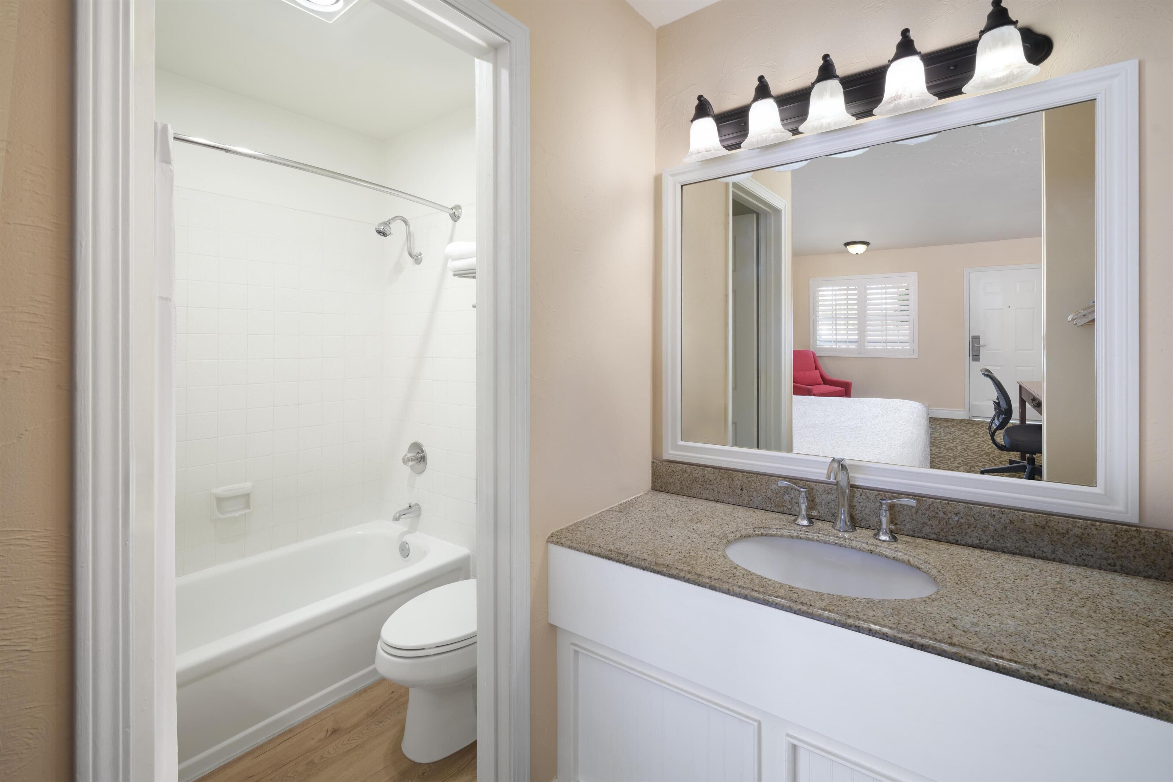 A bathroom with a white bathtub, toilet, and sink, a large mirror, and a light fixture above the mirror.