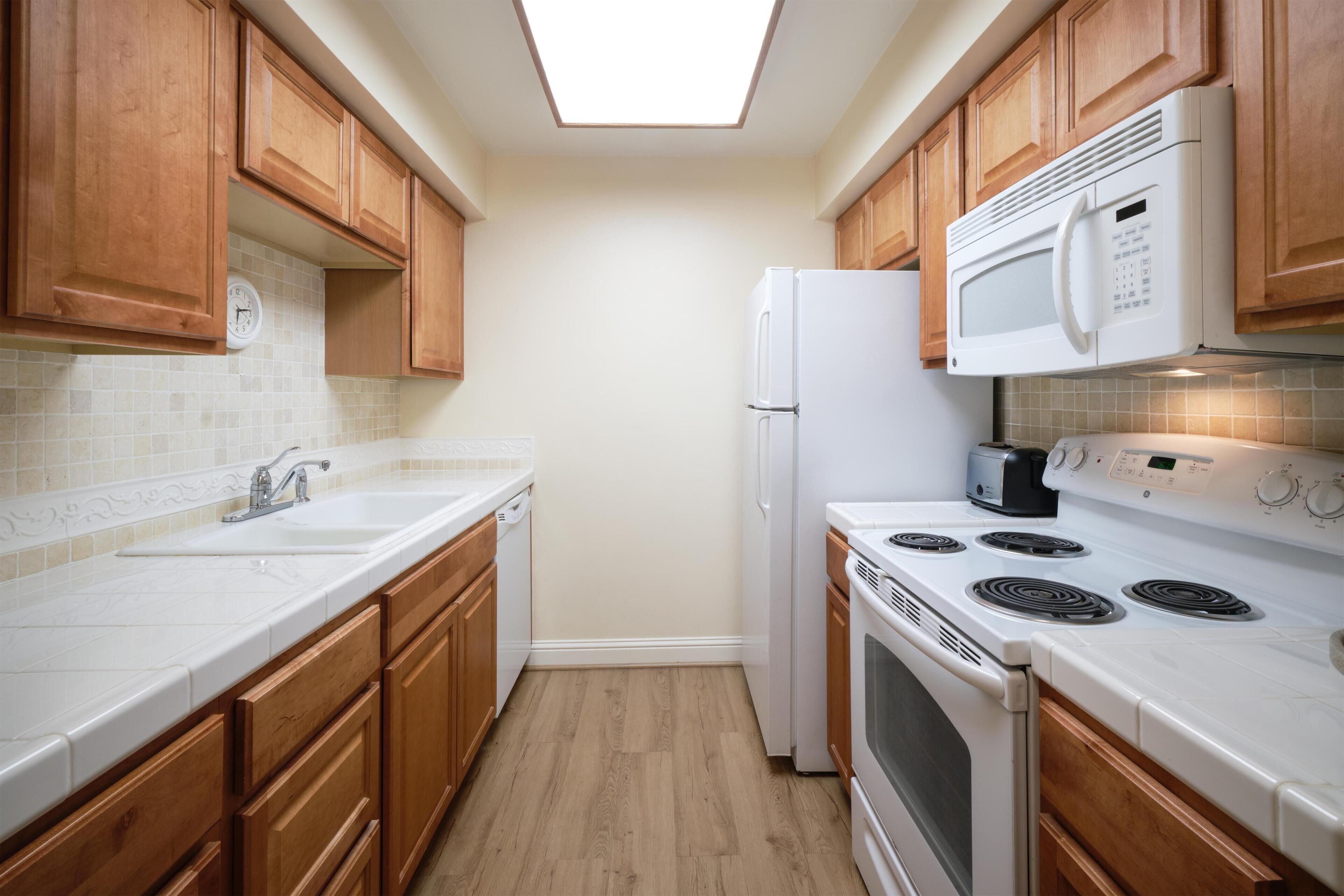 A kitchen with wooden cabinets, a white countertop, a built-in microwave, a stove, and a refrigerator.