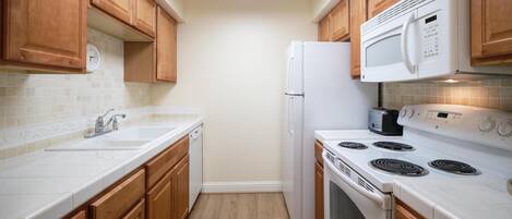 A kitchen with wooden cabinets, a white countertop, a built-in microwave, a stove, and a refrigerator.
