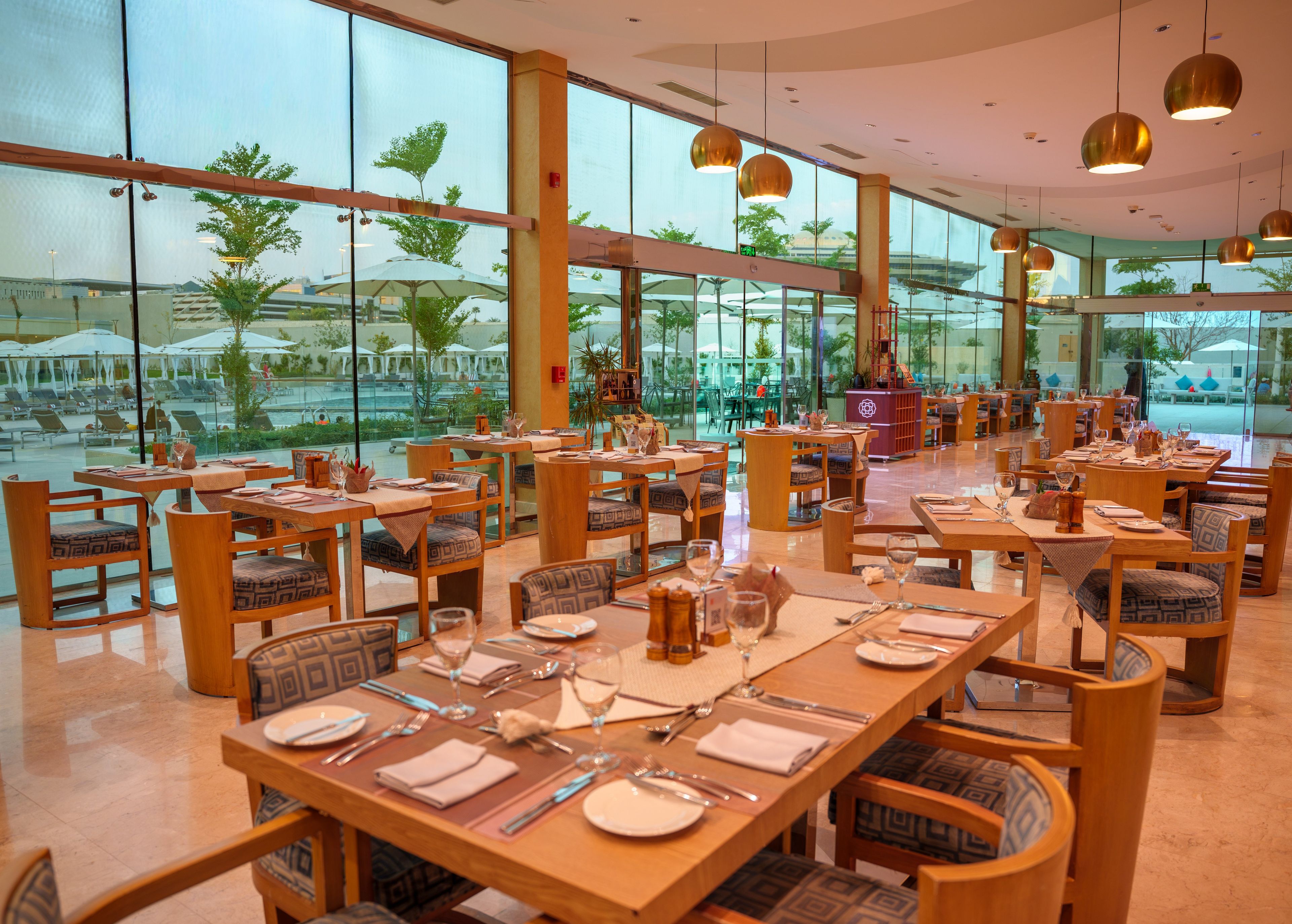 A restaurant with tables set for dining, large windows offering a view of the outdoor area, and pendant lighting.
