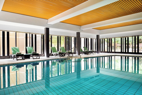 An indoor swimming pool with clear blue water, surrounded by lounge chairs and large windows.