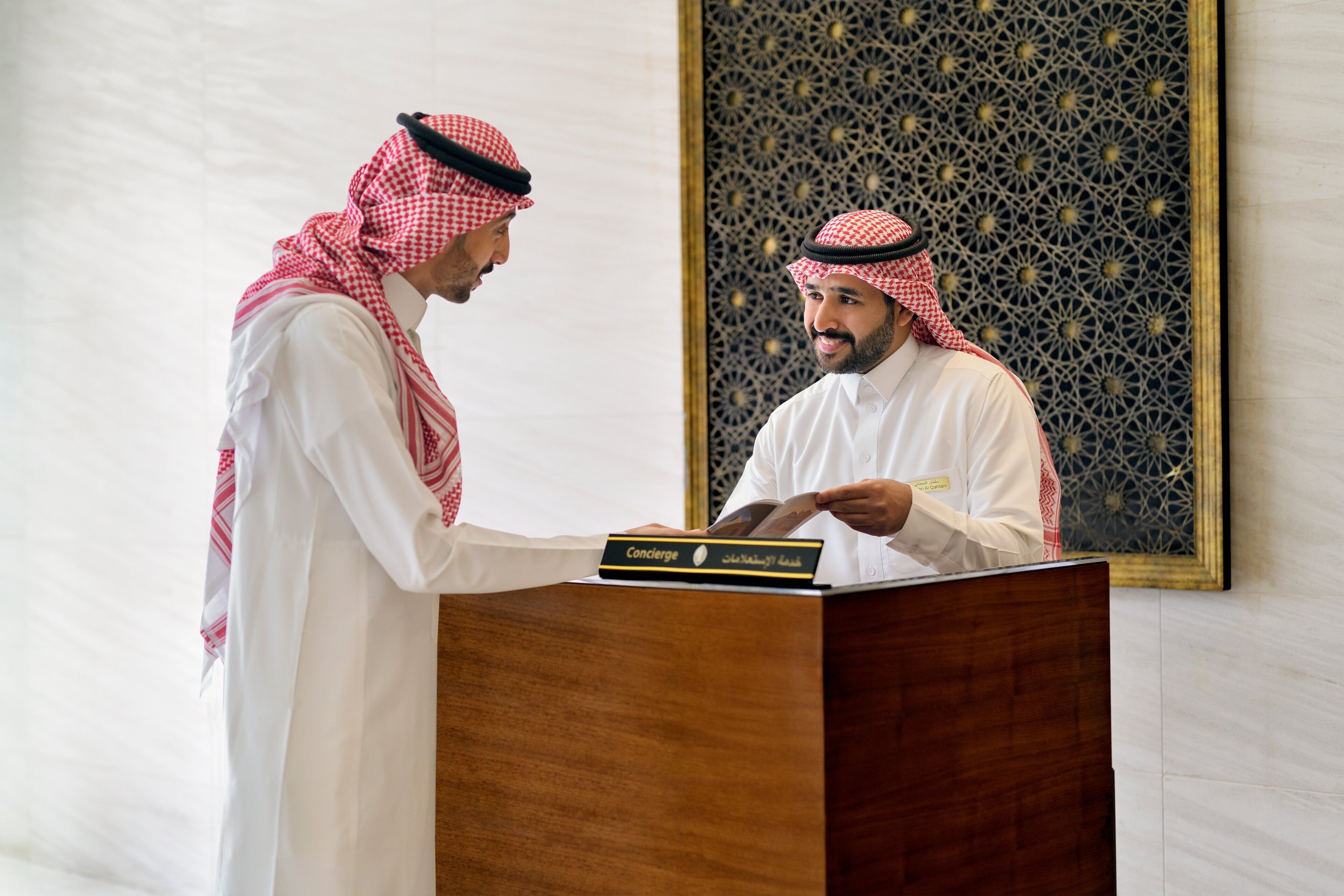 Two men in traditional attire at a wooden podium with a sign that reads "Concierge".