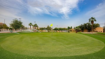 Un campo de golf bien cuidado con una bandera, palmeras y un cielo despejado.