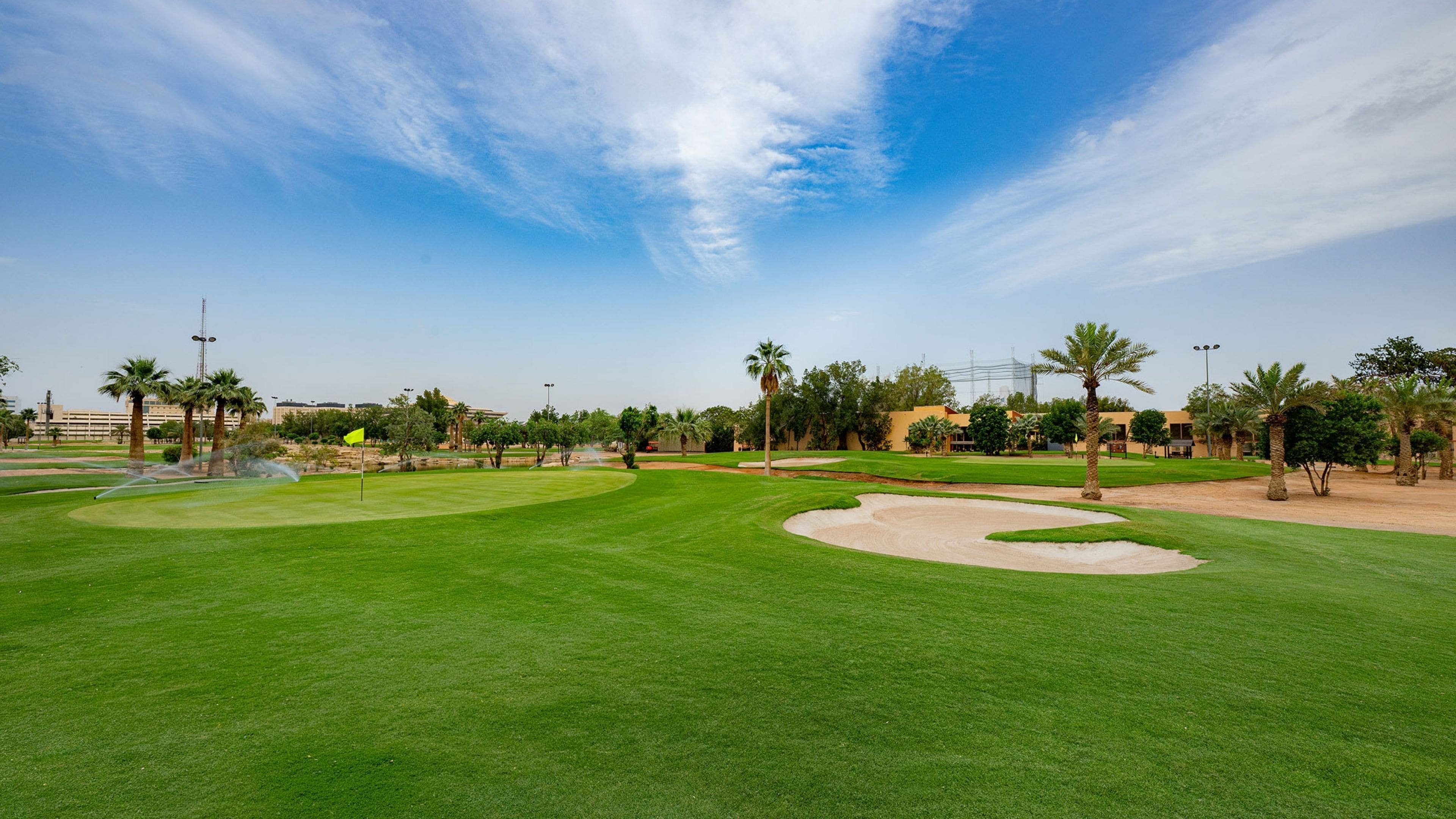 Campo de golf con búnkeres de arena, palmeras y cielo despejado.