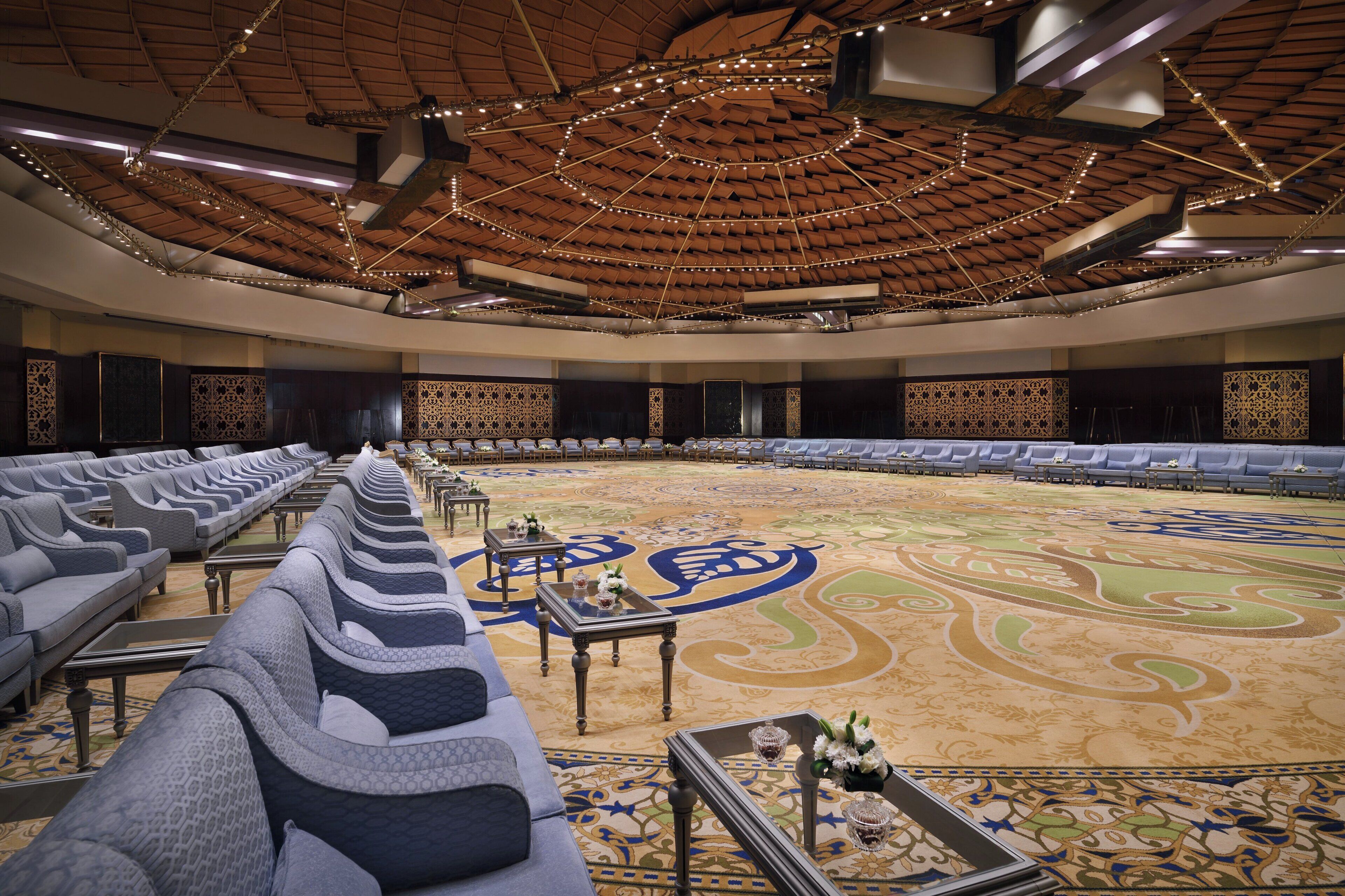 Une salle de conférence spacieuse, dotée de rangées de sièges, d’un tapis à motifs et d’un plafond haut agrémenté de luminaires.